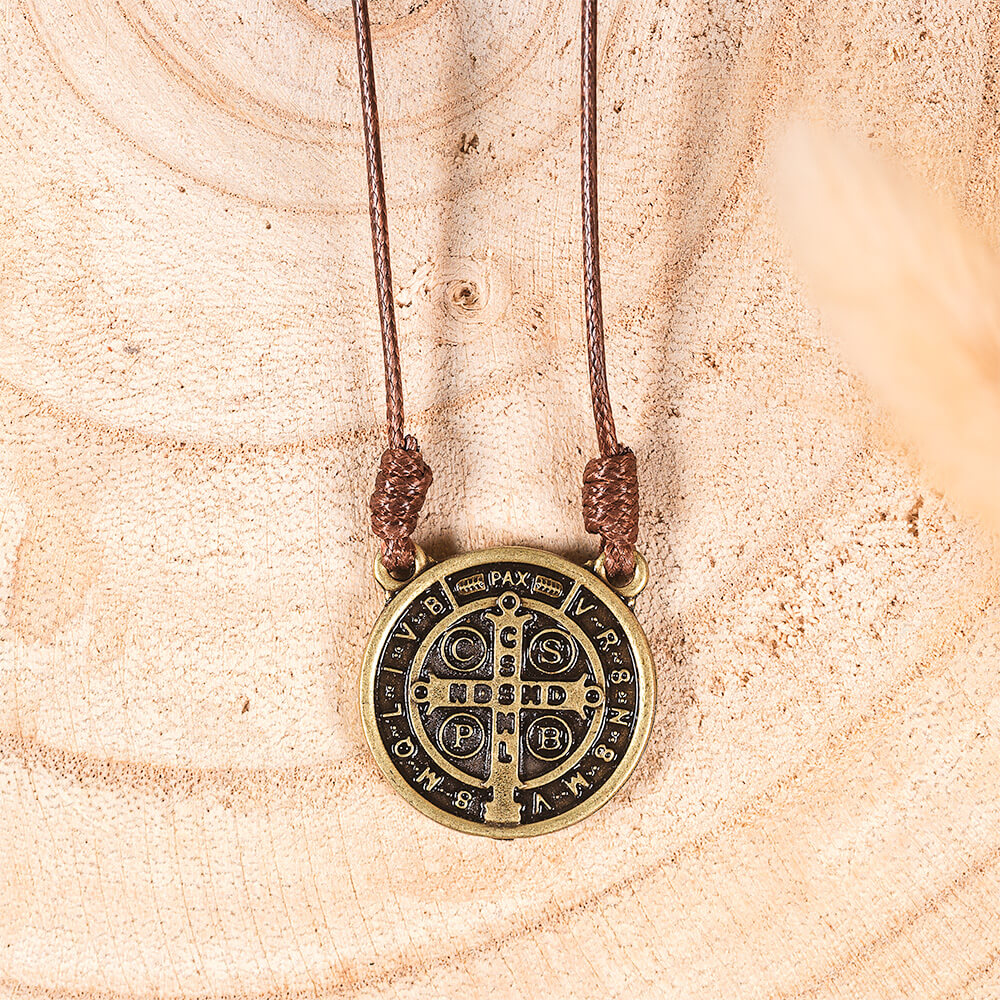 Saint Benedict medal necklace with brown cord and antique gold medallion on wood background.