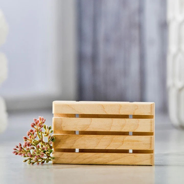 Wooden soap dish made of light-colored, horizontal slats with a flower accent on the side.