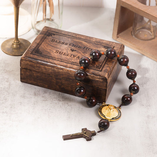 A wooden rosary box with a wooden rosary hanging off the side on a table with other items.