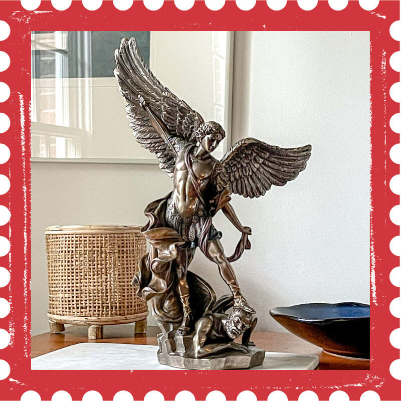 Bronze statue of St. Michael with outstretched wings on a wooden surface.