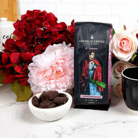 Bag of St. Valentine Catholic Coffee with chocolates and red and pink flowers on a countertop.
