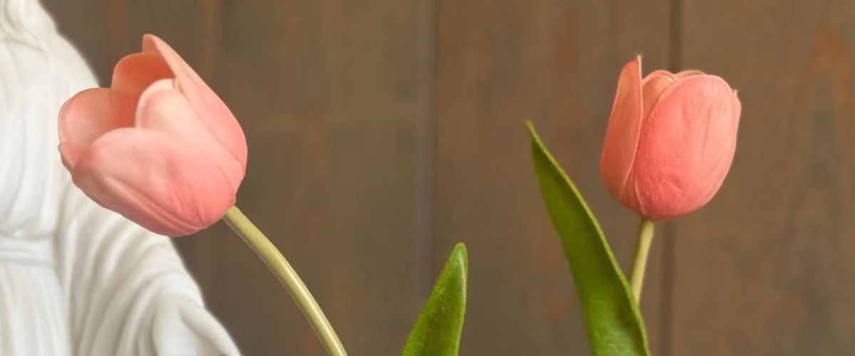 Two pink tulips in clear glass vases with small saint medal charms.