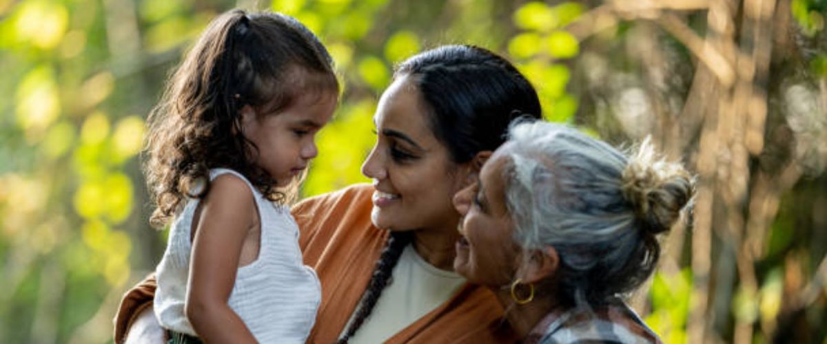Smiling mother and grandmother with a young child sharing a warm moment outdoors.