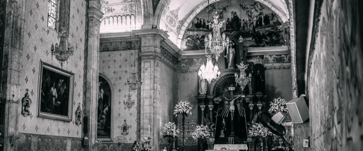 Black-and-white photo of a Catholic church interior with people seated in pews facing the altar during a service.
