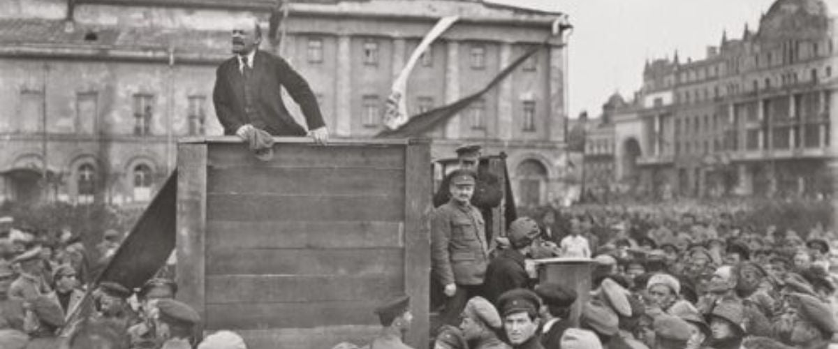 Black-and-white photo of a man speaking from a platform to a large crowd in a city square