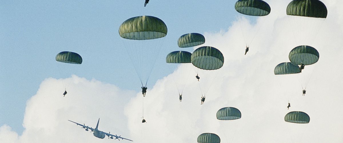 Paratroopers descending with green parachutes from a military aircraft against a cloudy sky