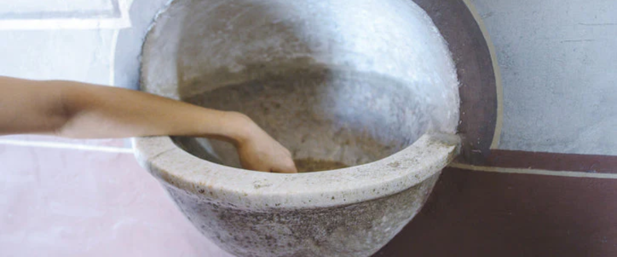 Hand reaching into a stone holy water font mounted on a wall.