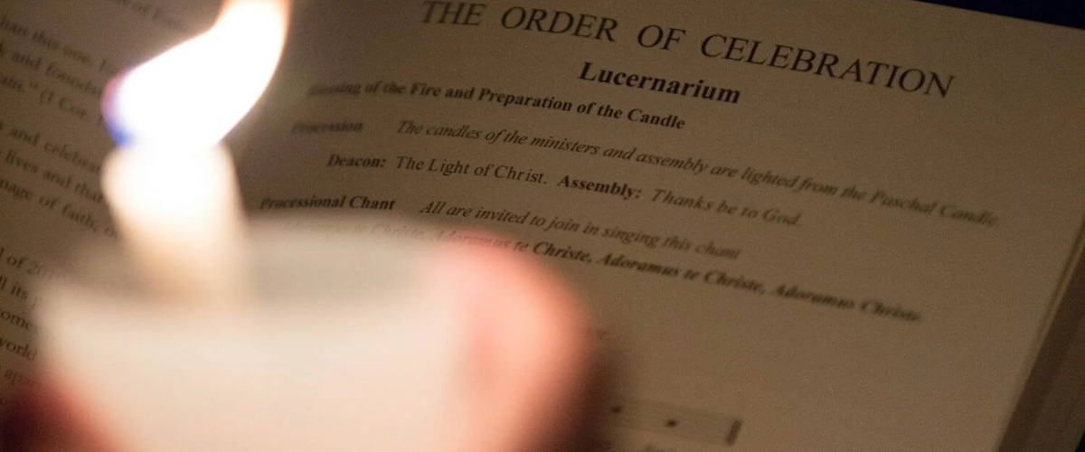 A lit candle in front of a church book showing the Order of Celebration