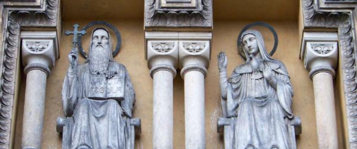 Stone statues of St. Benedict and St. Scholastica displayed on a church façade with columns between them