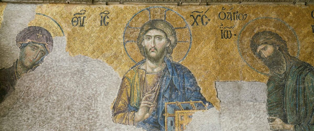 Ancient mosaic of Jesus Christ with gold background and halo, holding a book and giving a blessing gesture