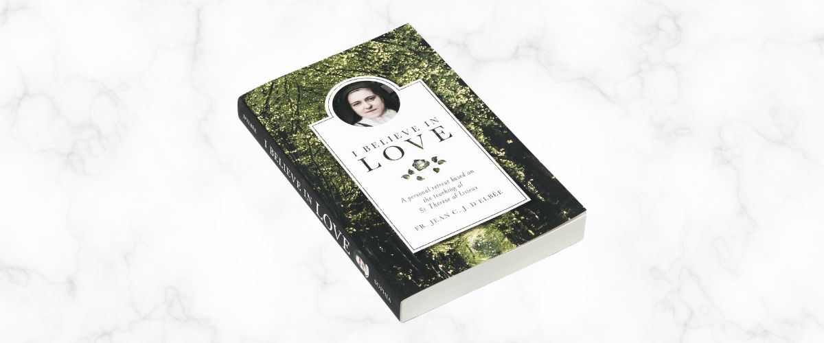 Book titled “I Believe in Love” by Fr. Jean C.J. d’Elbée resting on a marble surface with a forest-themed cover featuring St. Thérèse of Lisieux