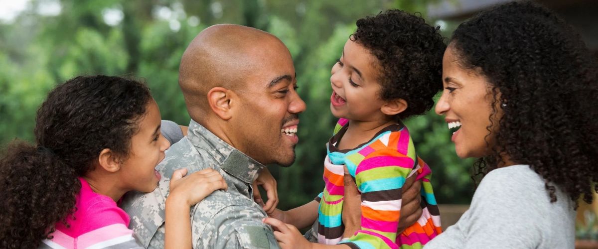 Smiling military father in uniform playing with his children while their mother looks on outdoors