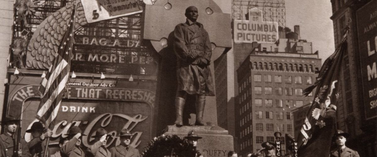 Historic black-and-white photo of a statue dedication ceremony in Times Square with officials, a large wreath, and vintage Coca-Cola and Columbia Pictures billboards in the background.