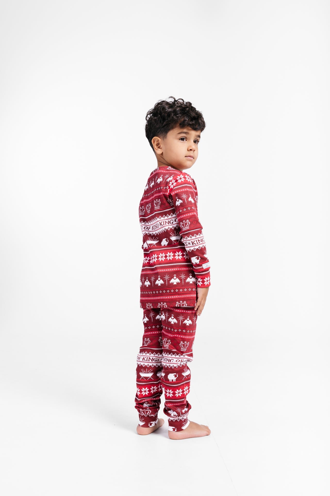 Child wears festive red pajama set with Christmas-themed patterns and "King of Kings" text design.