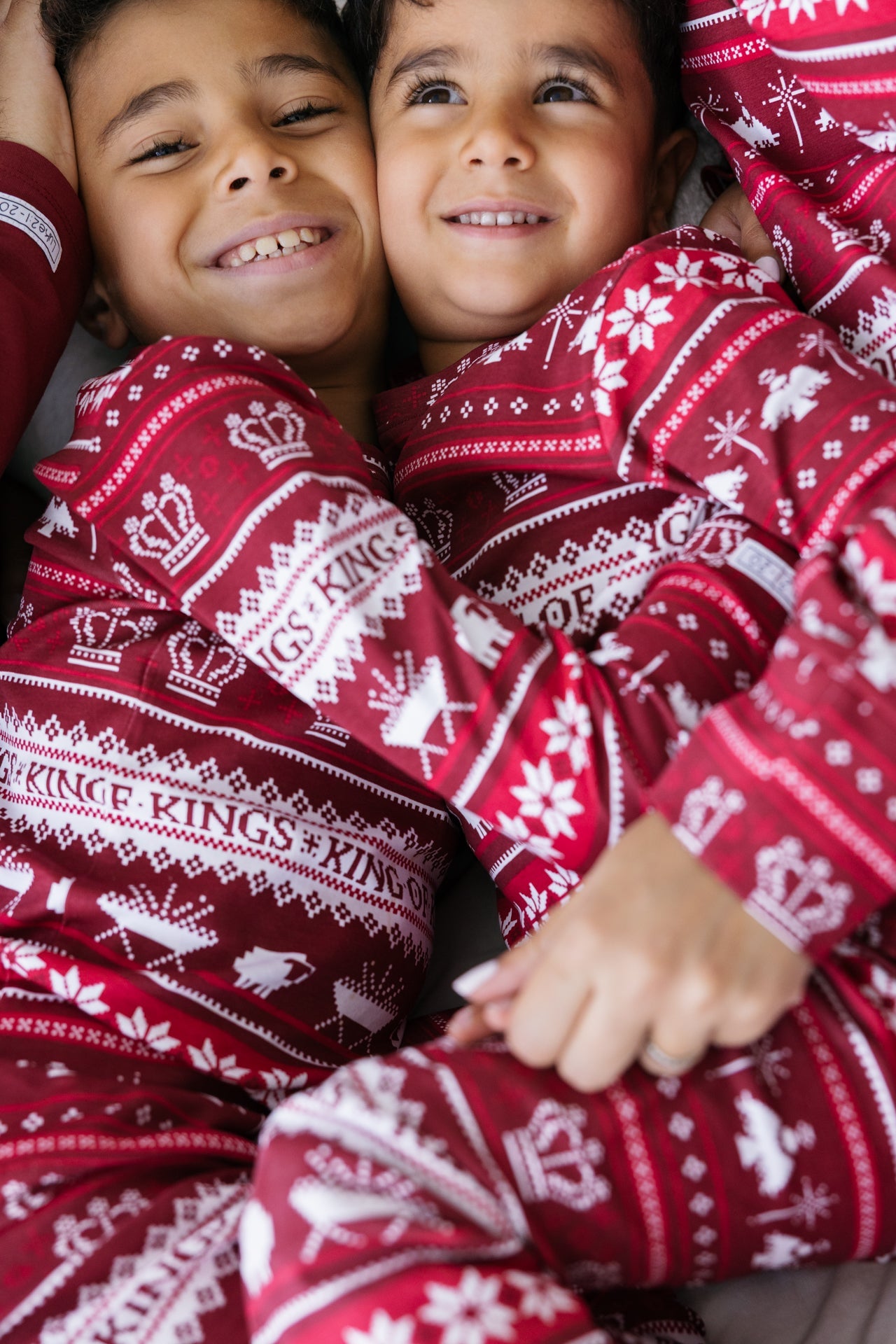 Matching Red and white patterned cotton pajamas on two smiling children, crown and snowflake design.