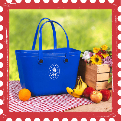Blue Marian tote bag with a logo on a tablecloth with fruits and flowers outdoors