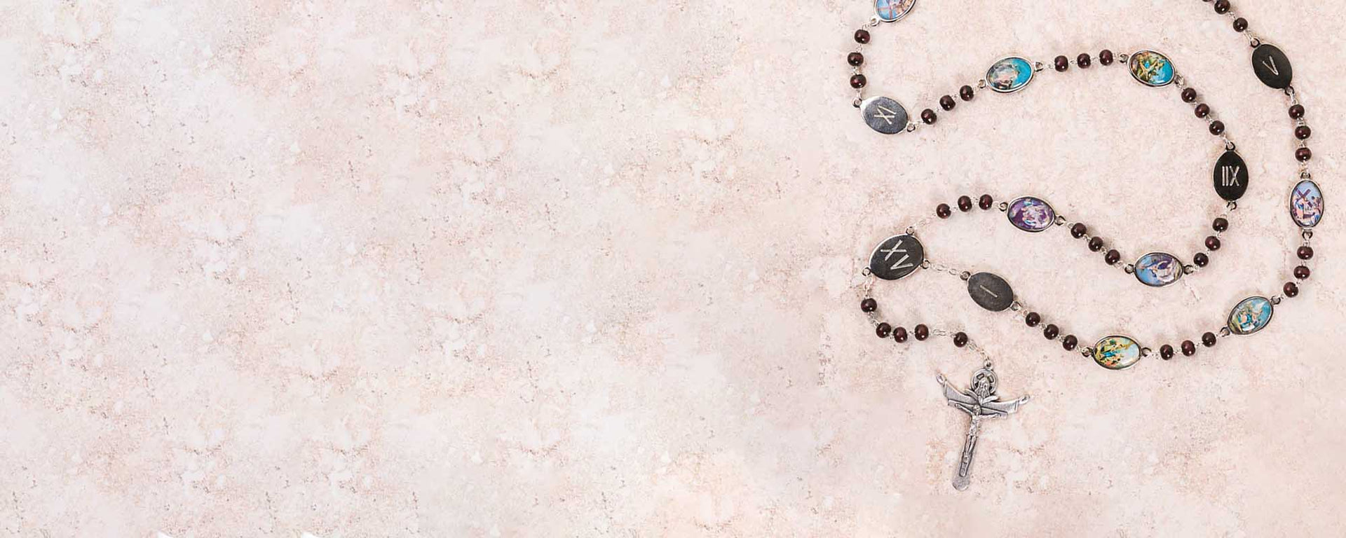 Rosary beads with illustrated medallions and a crucifix on a light stone background.