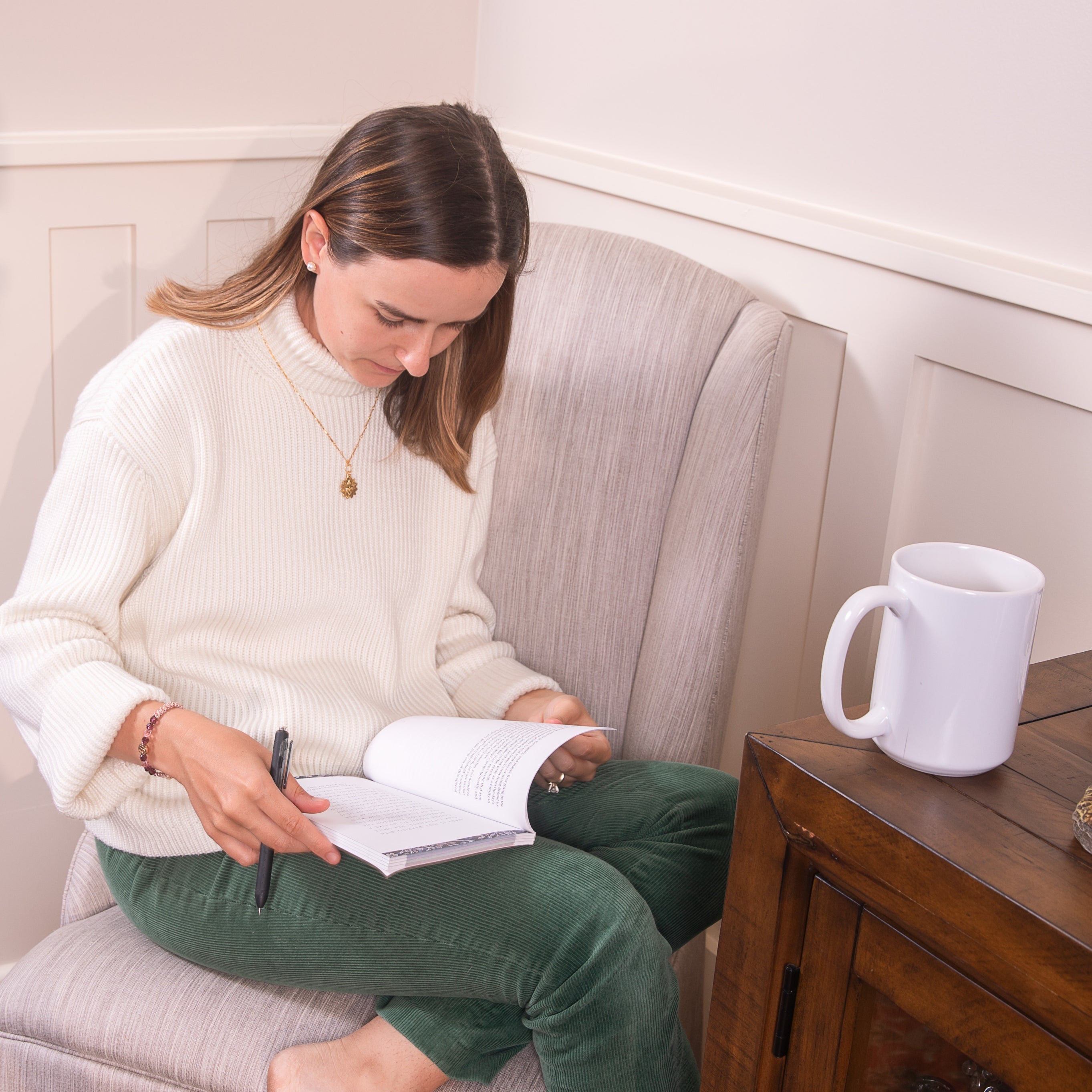 Woman sitting on a couch writing in a notebook with a mug next to her.