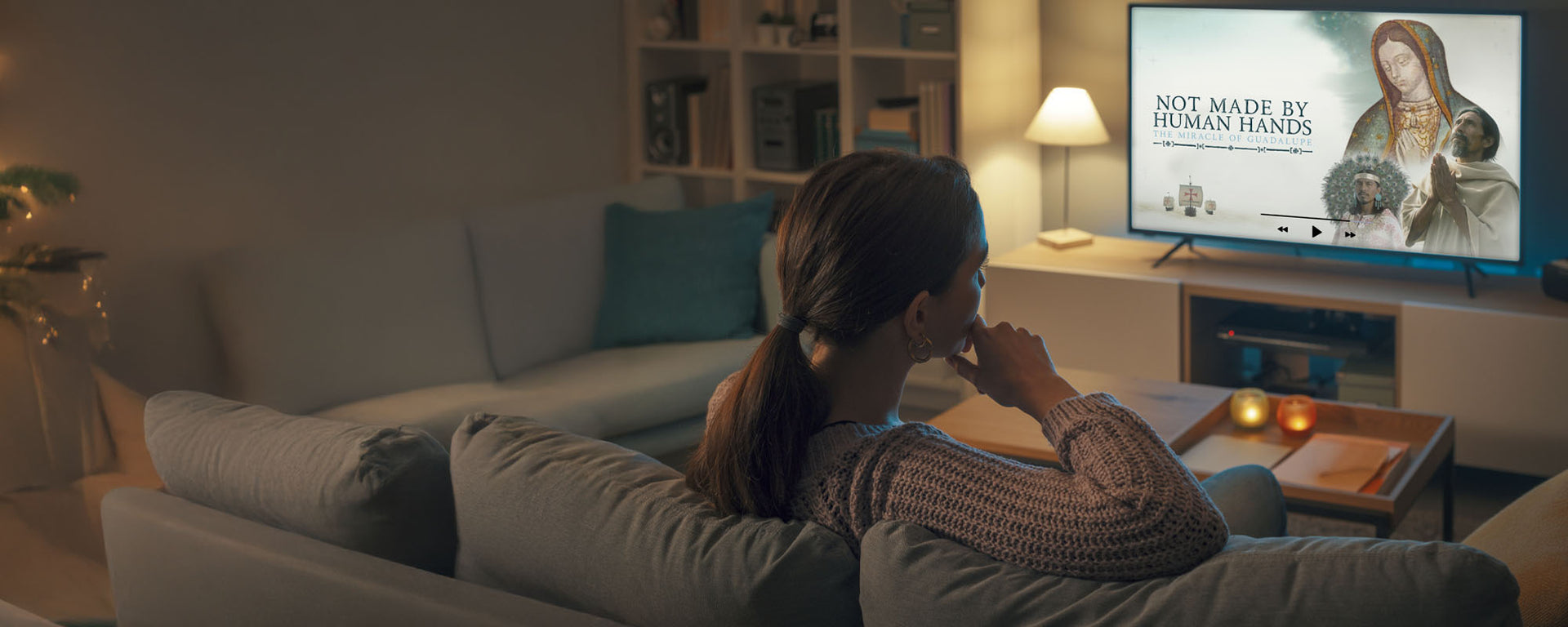 Woman on a sofa watching Not Made By Human Hands on TV in a cozy living room.