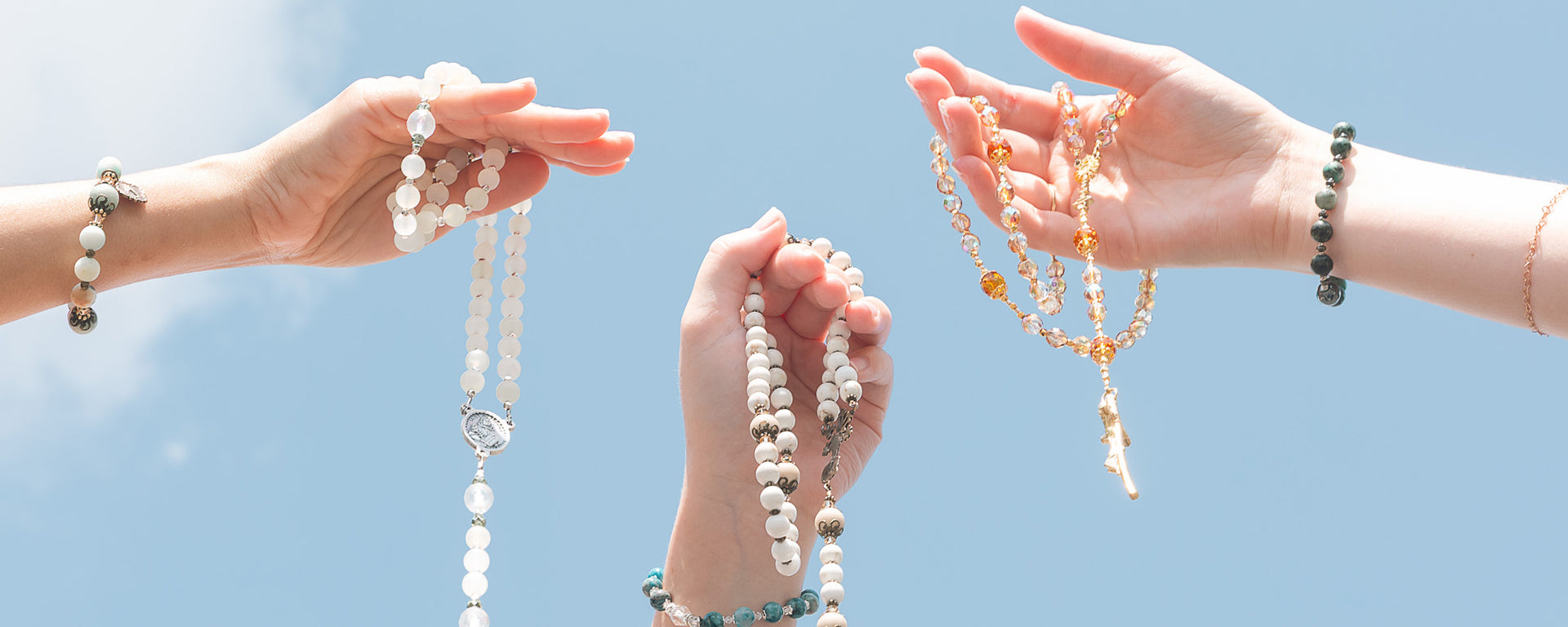 Hands holding rosary beads against a blue sky background.
