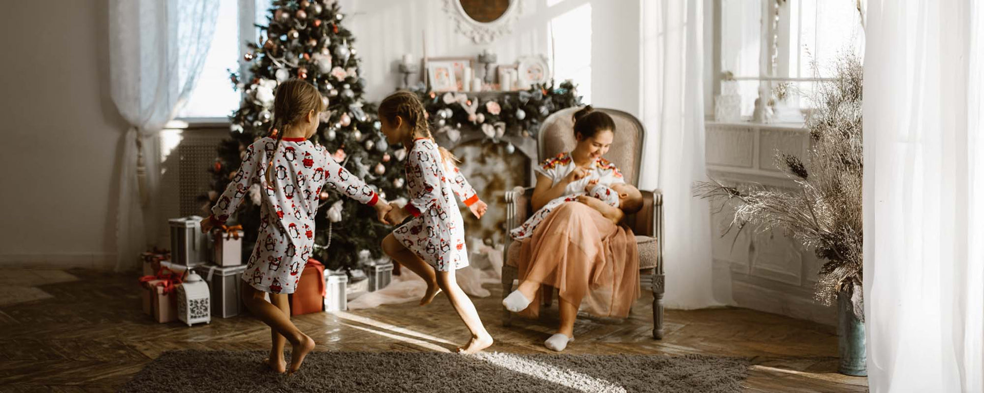 Family with children in festive pajamas by a Christmas tree, mother holding a baby.