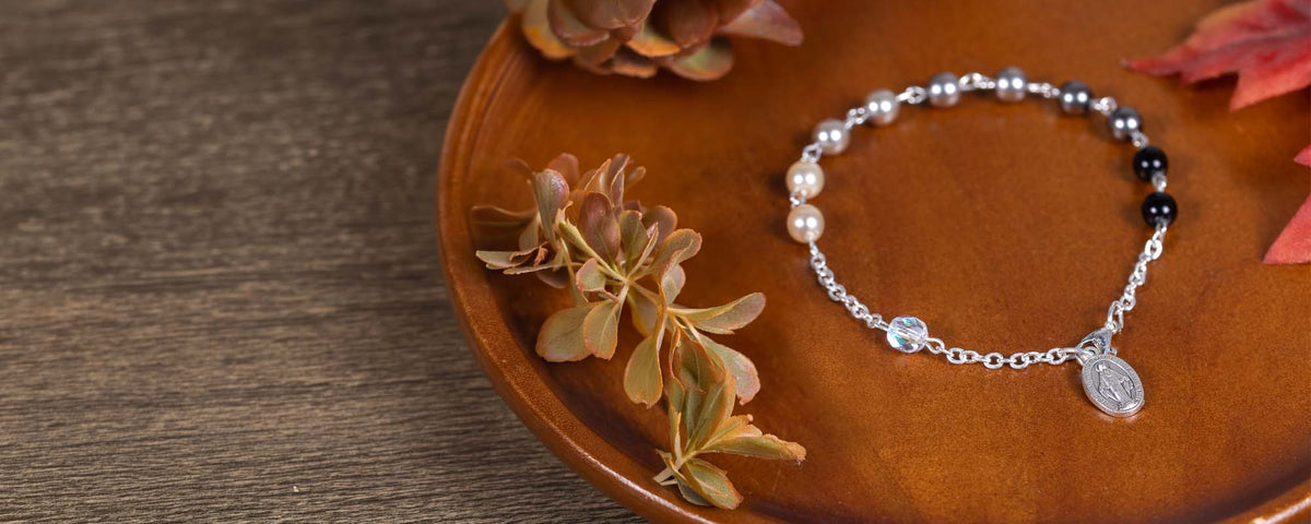 Black and white rosary bracelet on a wood backdrop in a lifestyle setting surrounded by fall foliage. 