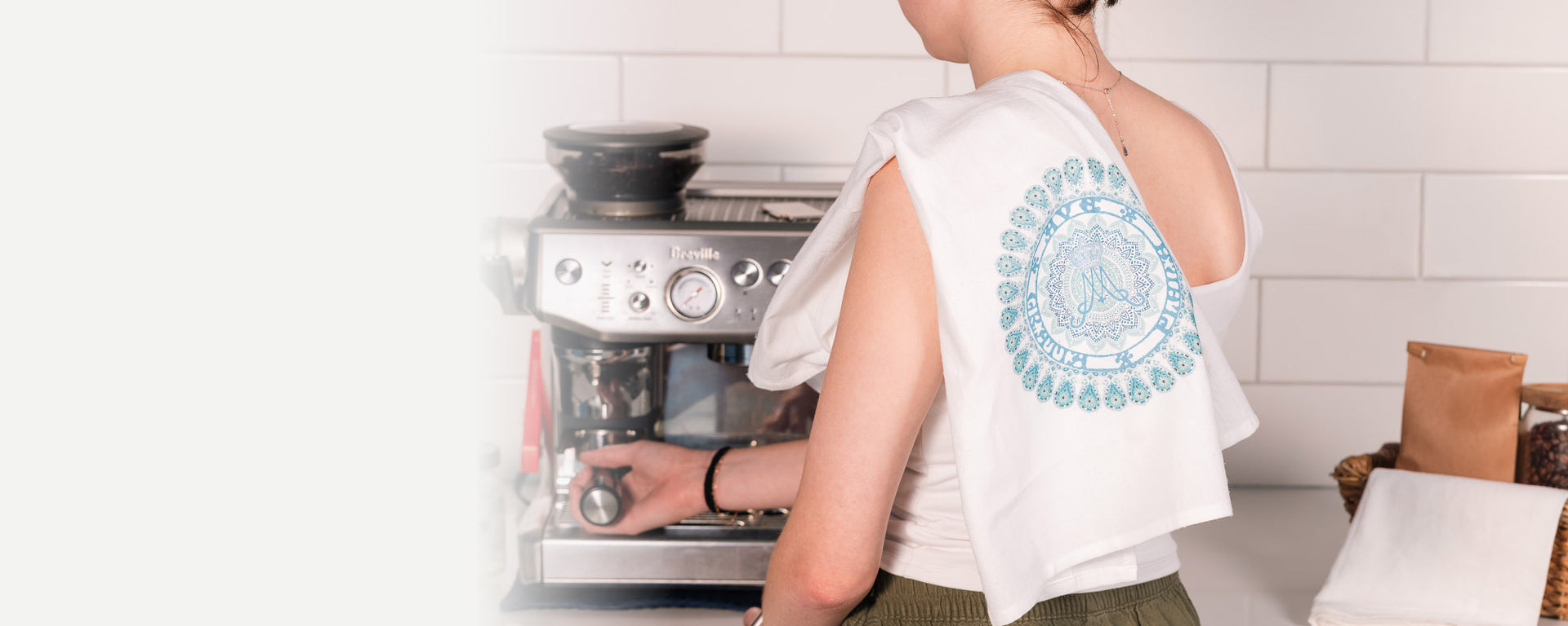 Person using a coffee machine in a kitchen setting with a dish towel on their shoulder.