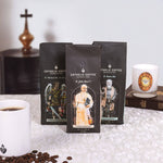 Three coffee packages labeled 'Catholic Coffee' with religious figures on a table with coffee beans and a cup.