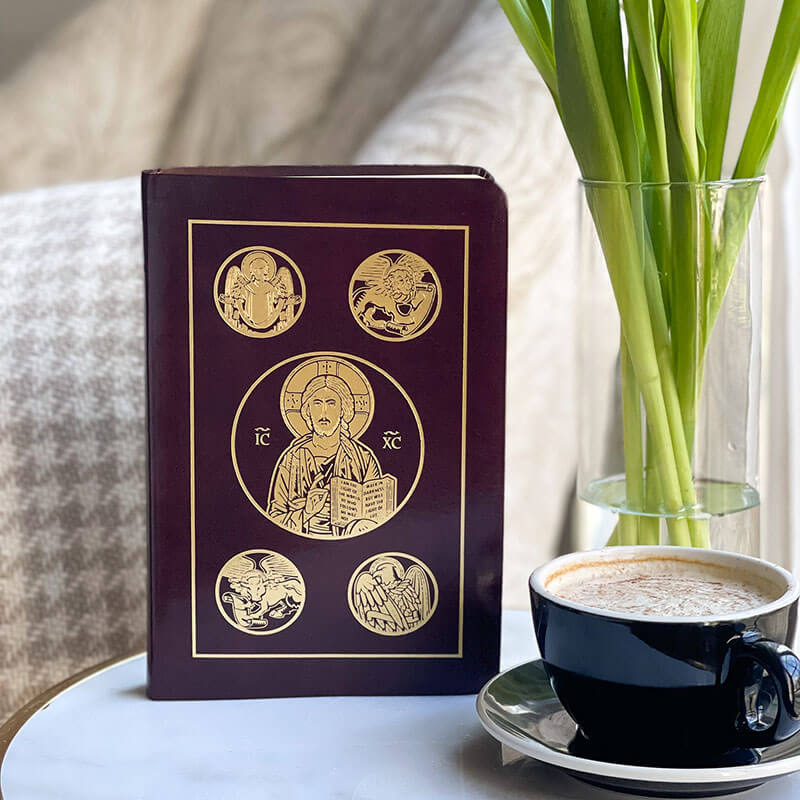 Decorative bible with religious symbols next to a cup of coffee on a table.