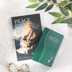 Two books titled 'Peace Be With You' and 'Healing Prayers for Every Day' on a marble surface with green leaves.