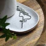 Silver crucifix necklace on a white ceramic dish with a wooden surface.
