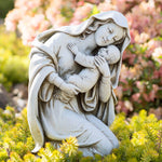 Statue of a woman holding a child in a garden setting