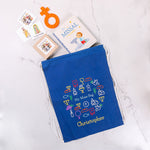 Blue drawstring bag with embroidered designs and text, placed on a white surface with religious books and cards.