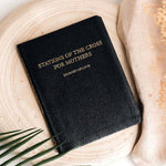Black book titled 'Stations of the Cross for Mothers' on a textured surface with a plant leaf.