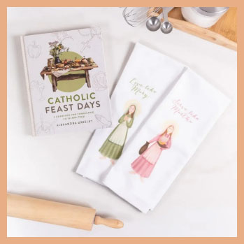 Catholic Feast Days book on a table with two while towels, a rolling pin and kitchen utensils in the background.