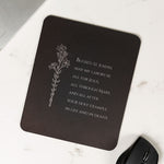 Black mouse pad with white text and floral design on a marble surface.