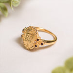 Gold ring with intricate design and small gemstones on a light background.