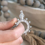 Silver rosary ring held by a hand with blurred background.