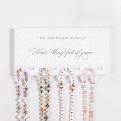 Set of rosary beads displayed on a holder with 'The Anderson Family' and 'Hail Mary full of grace' text on a white background.