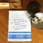 Tea towel with a Mother Teresa quote on a wooden surface with kitchen items.