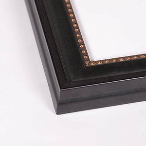 Close-up of a black picture frame corner with a decorative border of small metallic studs and gold-toned floral accents, shown on a white background.