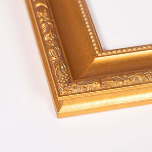 Close-up of an ornate gold picture frame corner with carved floral and beaded details, photographed on a plain white background.