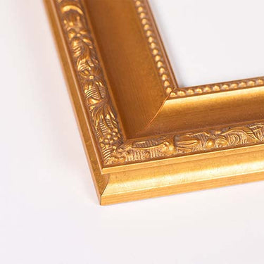 Close-up of an ornate gold picture frame corner with carved floral and beaded details, photographed on a plain white background.