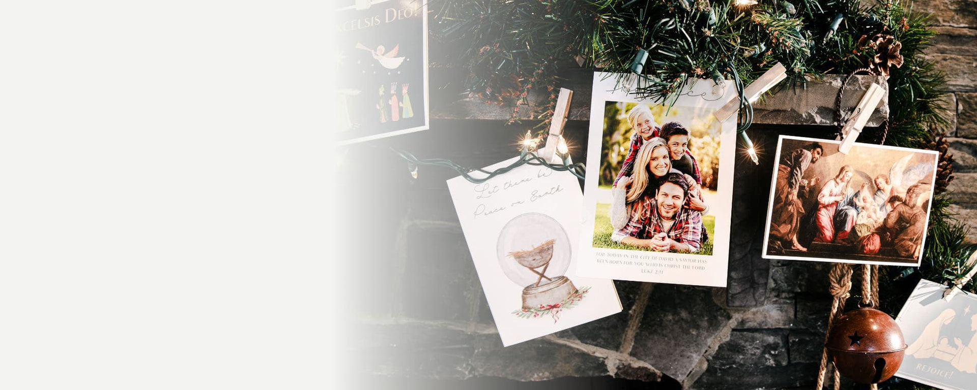 Christmas cards hanging on a decorated mantel with greenery and lights.