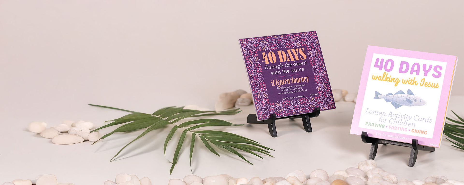 Two Lenten devotional books displayed on stands with palm leaves and stones.
