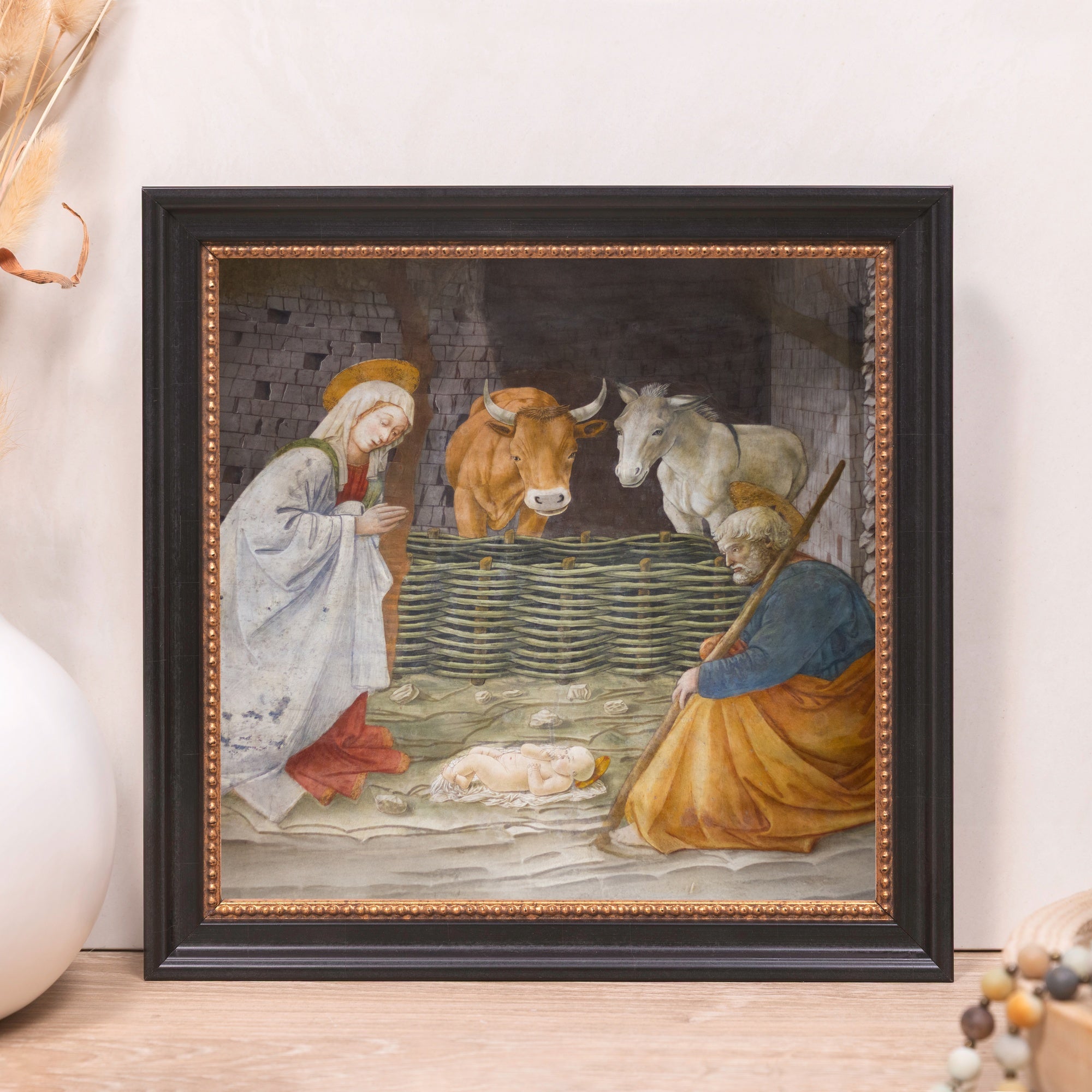 Framed Nativity scene art print with Mary, Joseph, baby Jesus, and livestock in black and gold frame.