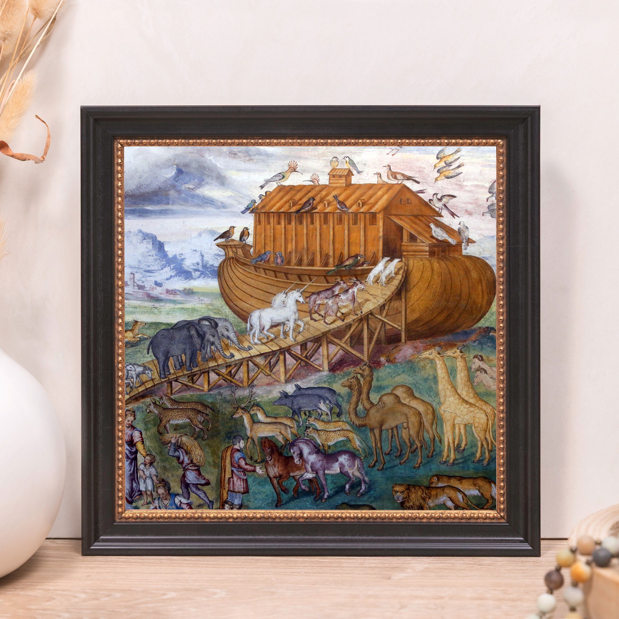 Framed print depicting Noah's Ark and animals, with a brown ark, mountains in the background, and a black frame.
