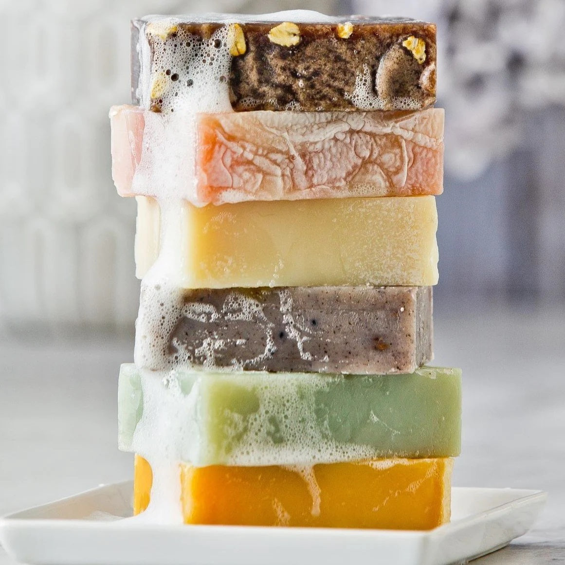 Stacked soaps in a variety of colors and textures including brown, peach, yellow, gray, green, and orange.