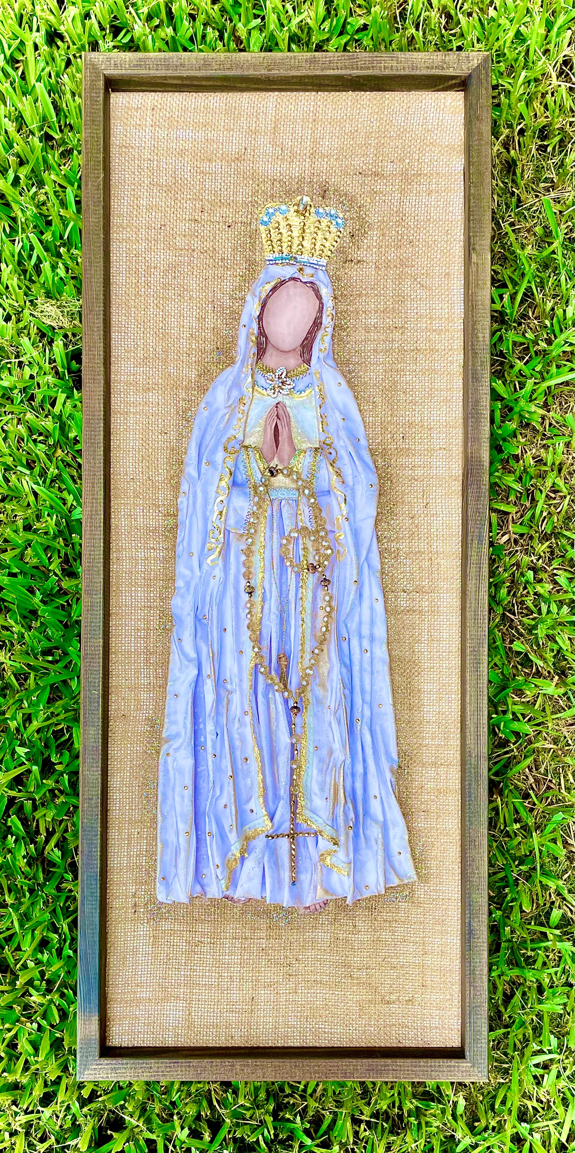 Framed burlap art of Virgin Mary wearing a blue and gold robe and a crown, holding a rosary.
