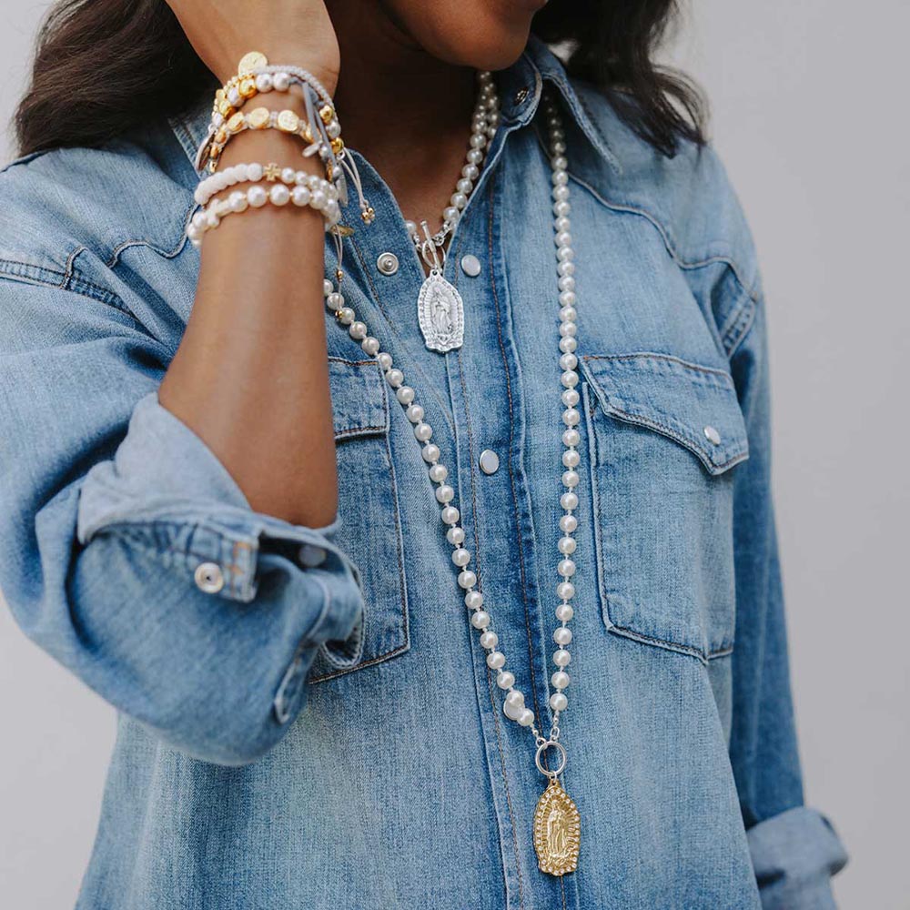 Woman wears pearl necklaces and bracelets with Virgin Mary pendants on a denim shirt.